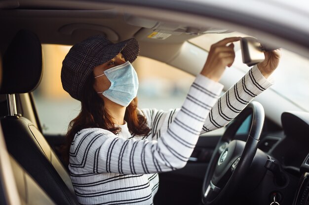 Mujer taxista ajusta el espejo retrovisor con máscara médica estéril