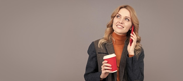 Mujer con taza de café Chattering chica hablar en el teléfono móvil bebiendo café fondo gris chatterbox retrato de mujer estandarte de encabezado aislado con espacio de copia