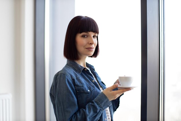 Mujer con taza de café disfrutando de la vista desde la ventana panorámica