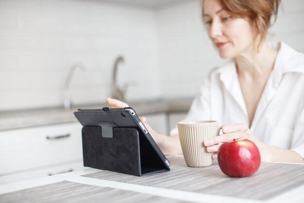 Mujer con taza de café o té usando la computadora portátil en casa