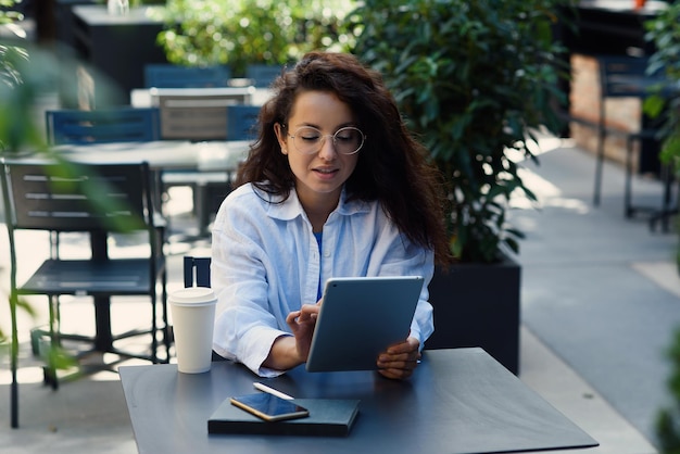 Mujer con taza de café trabajando en un café al aire libre por la mañana