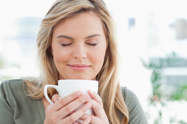 Mujer con taza elevada cerca de su boca, ojos cerrados y sonriendo