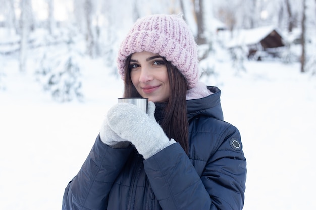 Mujer con taza de té caliente en el parque nevado en invierno