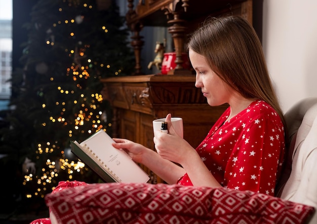 Mujer con taza de té en las manos sentado en una silla en casa acogedora con abeto en las vacaciones de Navidad