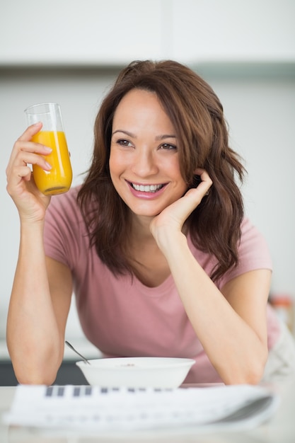 Mujer con un tazón de cereales, jugo de naranja y periódico en la cocina