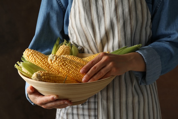 Mujer con tazón de maíz fresco contra marrón