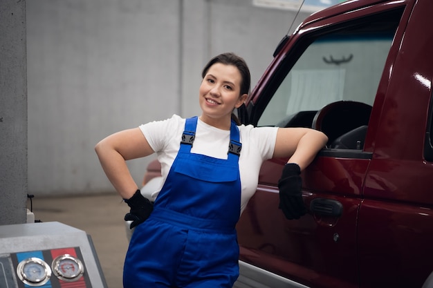 Una mujer técnica con un mono azul está parada en el coche.