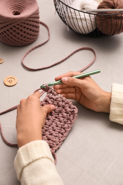 Mujer tejiendo con hilos en el primer plano de la mesa gris