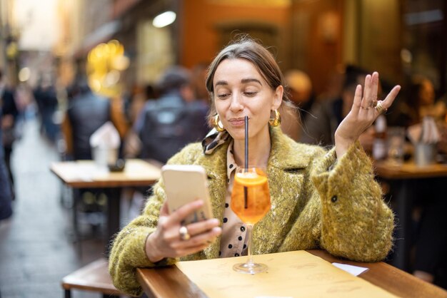 Mujer con teléfono y bebida en el bar al aire libre
