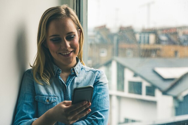 Mujer con teléfono en casa junto a la ventana.