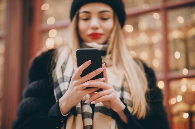 Mujer con teléfono celular en clima frío afuera en calles urbanas