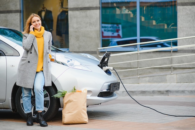 Mujer con teléfono cerca de un coche eléctrico de alquiler