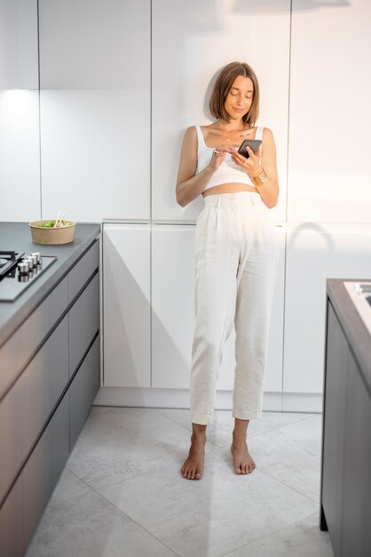 Mujer con teléfono en la cocina moderna en casa
