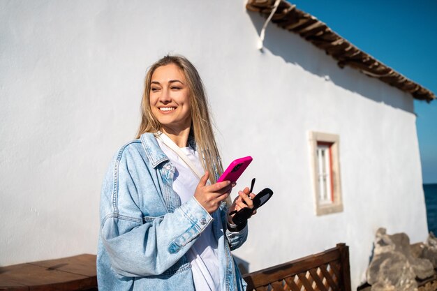 Mujer con teléfono y gafas fuera del hotel frente a la playa