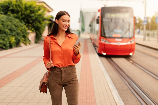 Foto una mujer con un teléfono inteligente compra boletos de tranvía en la parada de la ciudad