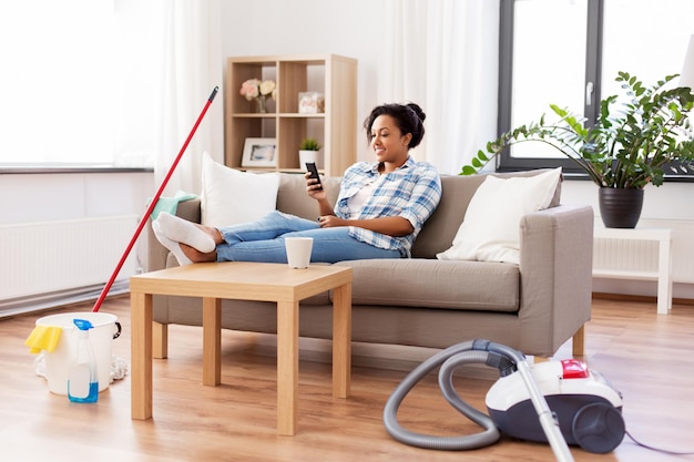 mujer con teléfono inteligente descansando después de la limpieza de la casa