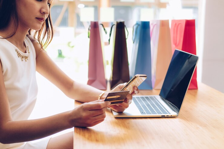 Mujer con teléfono inteligente móvil y tarjeta de crédito para pago en línea con bolsas de compras en la mesa