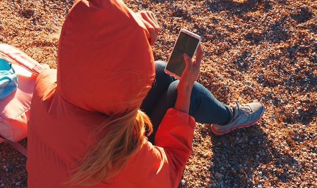 Mujer con un teléfono inteligente sentado en la playa al atardecer.