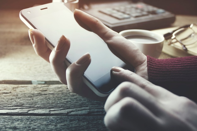 Mujer con teléfono inteligente y taza de café en la mesa de trabajo