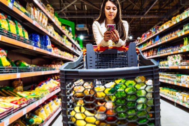 Mujer con teléfono inteligente en la tienda de comestibles y compras