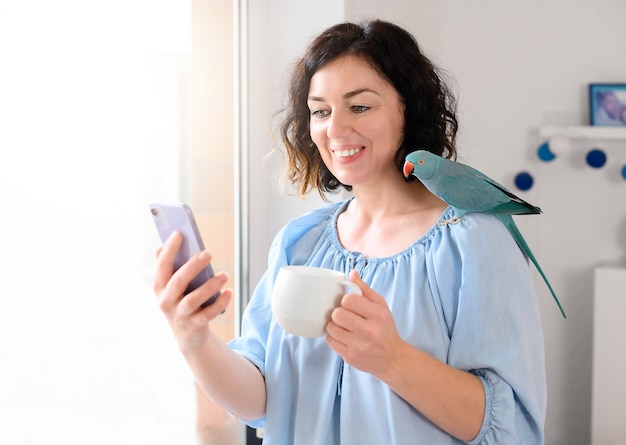 Mujer con teléfono con loro y taza de café.