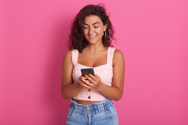 Mujer con teléfono móvil en manos, alegre joven sosteniendo teléfono inteligente y sonriendo