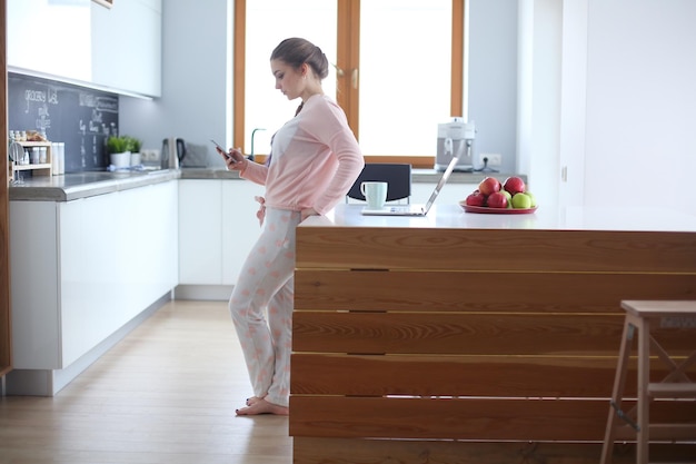 Mujer con teléfono móvil de pie en la cocina moderna