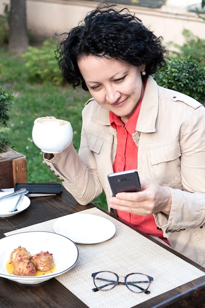 Una mujer con un teléfono móvil en sus manos se comunica en línea mientras está sentada en un café.