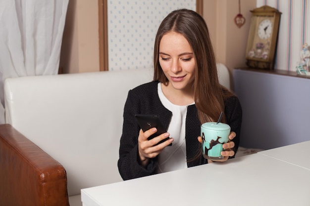 Mujer con teléfono móvil y taza de cóctel