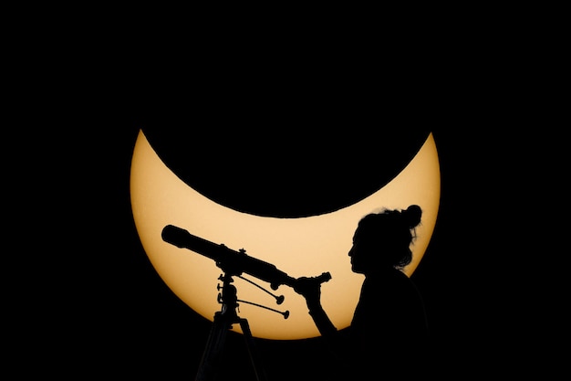 Foto mujer con telescopio observación segura del eclipse solar. sol real de fondo. observación del eclipse solar a través de un telescopio y un filtro especial para reducir la luz solar.