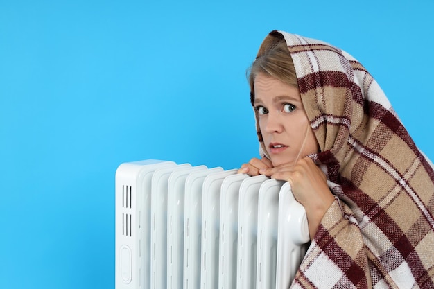 La mujer de la temporada de calefacción se calienta con un calentador sobre fondo azul.