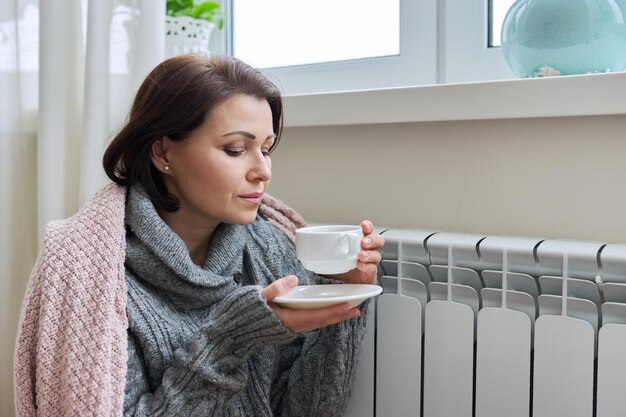 Mujer de la temporada de invierno calentándose cerca del radiador de calefacción del hogar