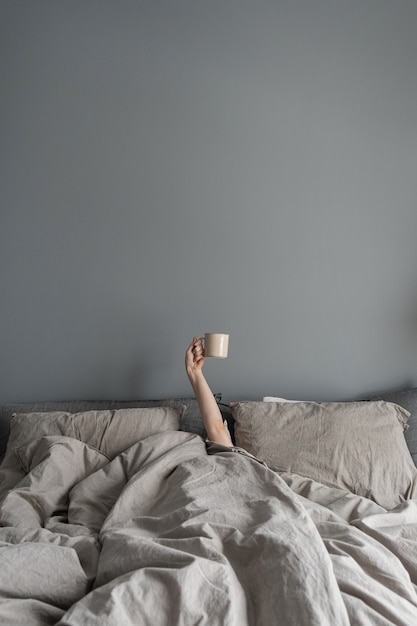 Mujer tendida en la cama y sosteniendo la taza con café con la mano