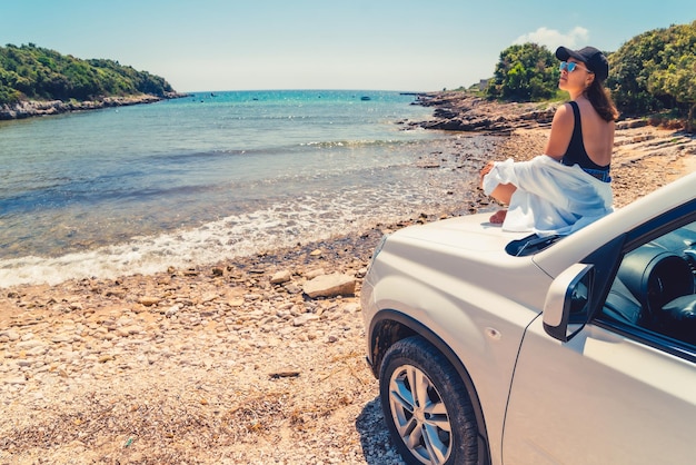 Foto mujer tendida en el capó del coche con vistas a la playa de verano del mar