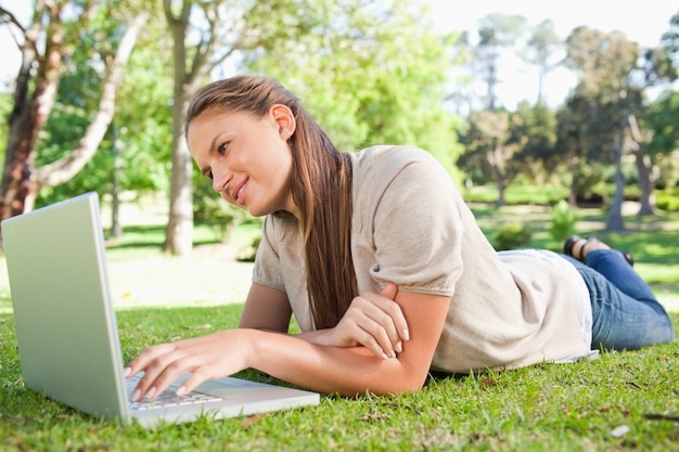 Mujer tendida en el césped con su computadora portátil