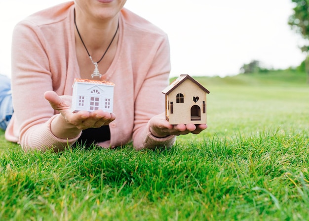 Foto mujer tendida en el pasto sosteniendo casas de juguete en sus palmas