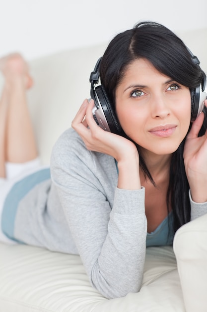 Foto mujer tendida en un sofá con los auriculares puestos