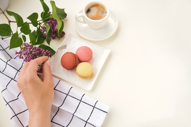 Mujer con tenedor, taza de café, macarrón de pastel en la mesa de luz desde arriba