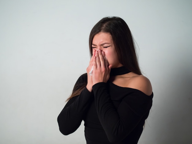 La mujer tiene alergia. Mujer en suéter negro sobre pared blanca