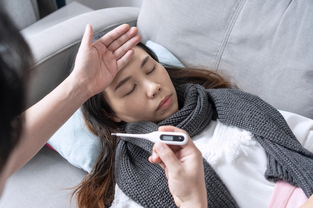 La mujer tiene fiebre acostada en el sofá mientras su marido mide la temperatura Concepto de problemas de salud