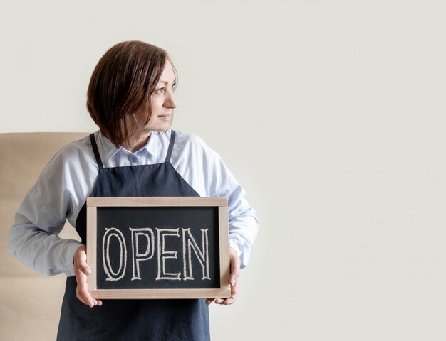 Mujer tiene tablero con texto abierto. Trabajador en delantal muestra la apertura de la cafetería o mercado.