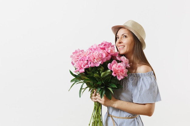 Mujer tierna joven en vestido azul, sombrero con ramo de hermosas flores de peonías rosas aisladas sobre fondo blanco. Día de San Valentín, concepto de vacaciones del Día Internacional de la Mujer. Área de publicidad.