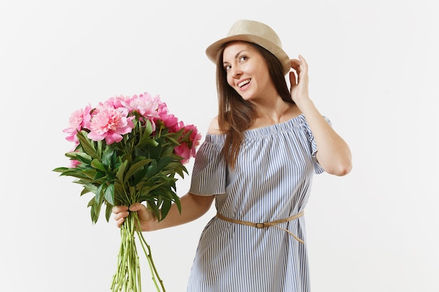 Mujer tierna joven en vestido azul, sombrero con ramo de hermosas flores de peonías rosas aisladas sobre fondo blanco. Día de San Valentín, concepto de vacaciones del Día Internacional de la Mujer. Área de publicidad.