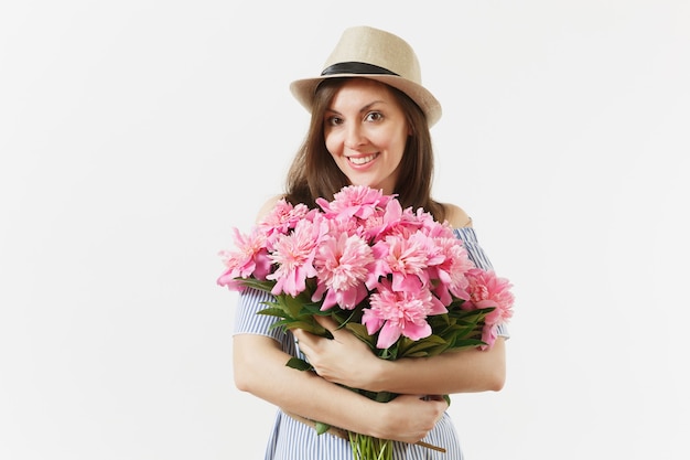 Mujer tierna joven en vestido azul, sombrero con ramo de hermosas flores de peonías rosas aisladas sobre fondo blanco. Día de San Valentín, concepto de vacaciones del Día Internacional de la Mujer. Área de publicidad.