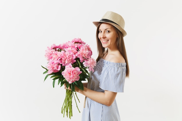 Mujer tierna joven en vestido azul, sombrero con ramo de hermosas flores de peonías rosas aisladas sobre fondo blanco. Día de San Valentín, concepto de vacaciones del Día Internacional de la Mujer. Área de publicidad.