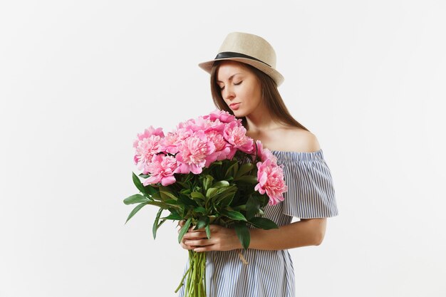 Mujer tierna joven en vestido azul, sombrero sosteniendo, oliendo ramo de flores de peonías rosas aisladas sobre fondo blanco. Día de San Valentín, concepto de vacaciones del Día Internacional de la Mujer. Área de publicidad.