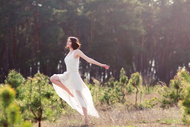 Mujer tierna en vestido blanco bailando en la naturaleza