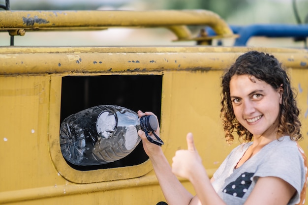 Mujer tirando basura en la papelera de reciclaje de plástico haciendo golpes.