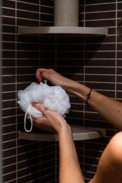 Mujer tirando jabón sobre una esponja blanca en la ducha del baño