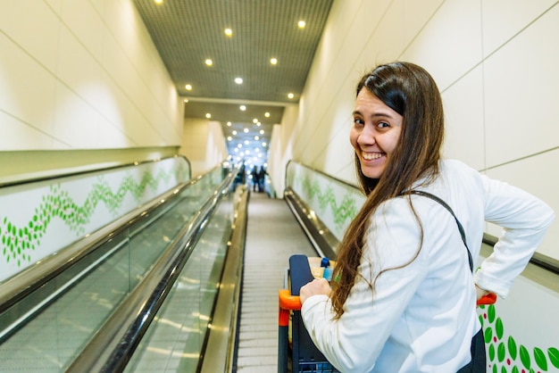 Mujer tire de la carretilla en la escalera mecánica. concepto de compras